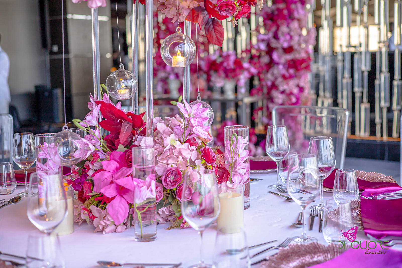 Hanging glass lanterns with candles above an arrangement of pink and red flowers, the crystal wall softly blurred behind