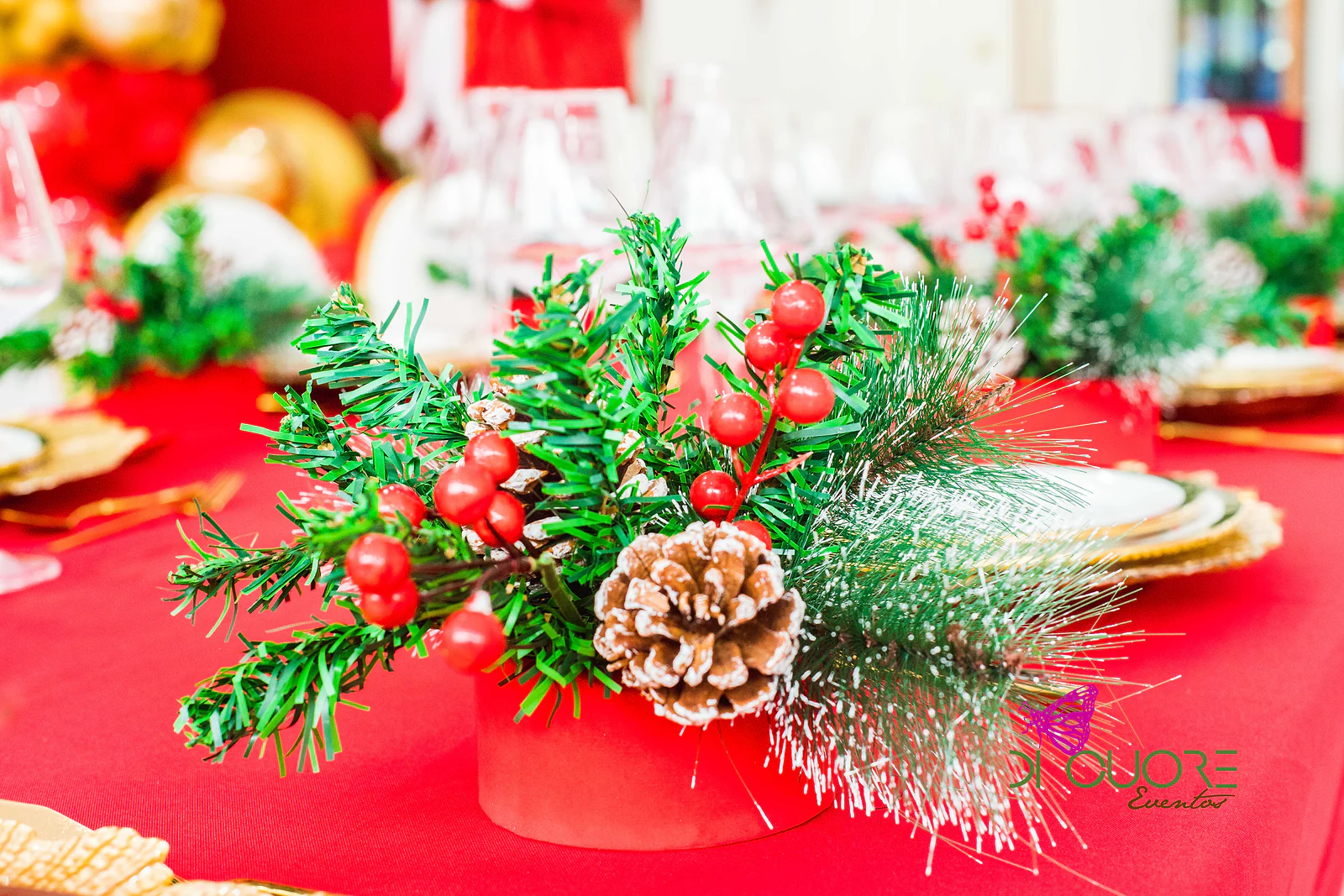 Pine arrangement with red berries and a pine cone on a red cloth, with gold plates softly blurred behind