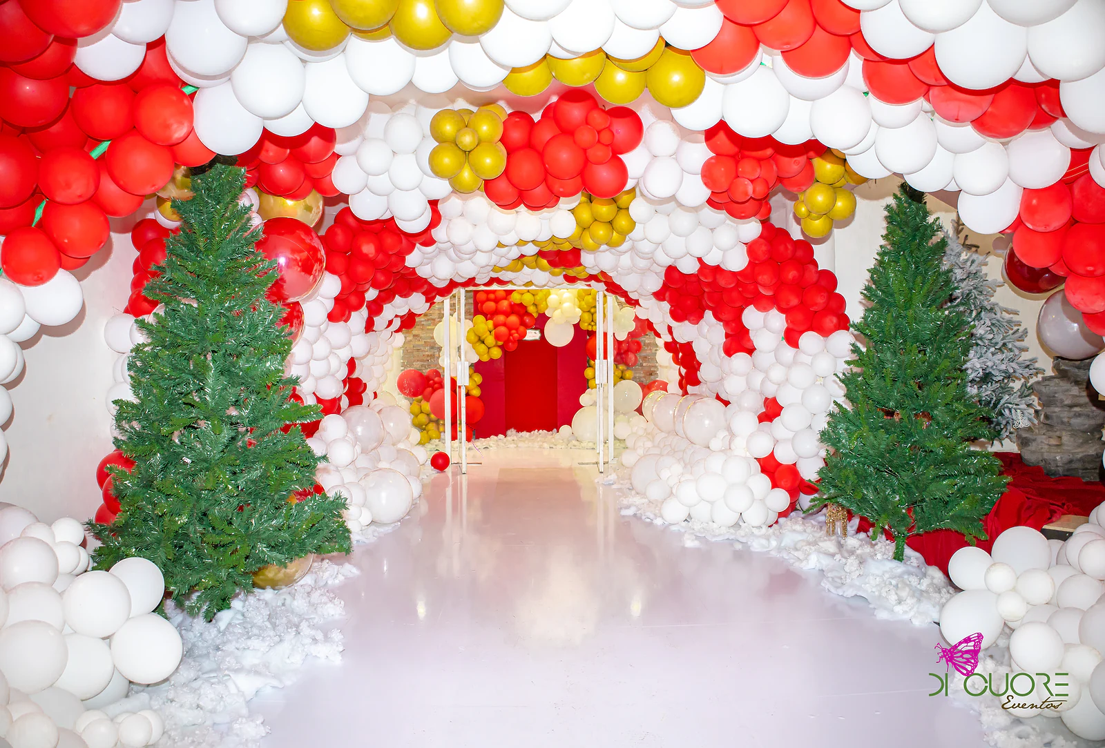 Tunnel of white, red and gold balloons with two Christmas trees, leading into the hall