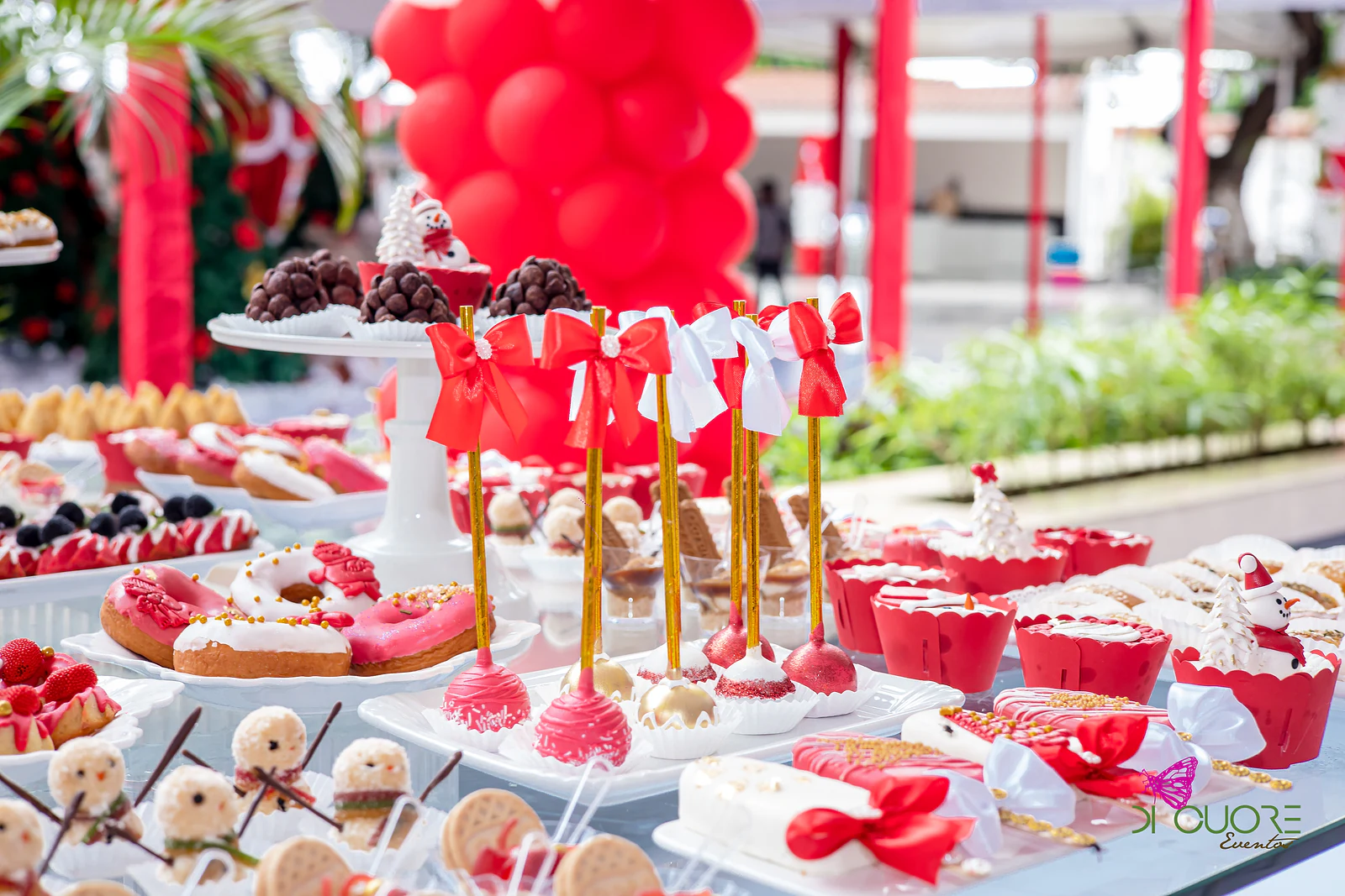 Christmas sweet table with red-bowed cake pops, doughnuts, cupcakes and snowmen, before a column of red balloons