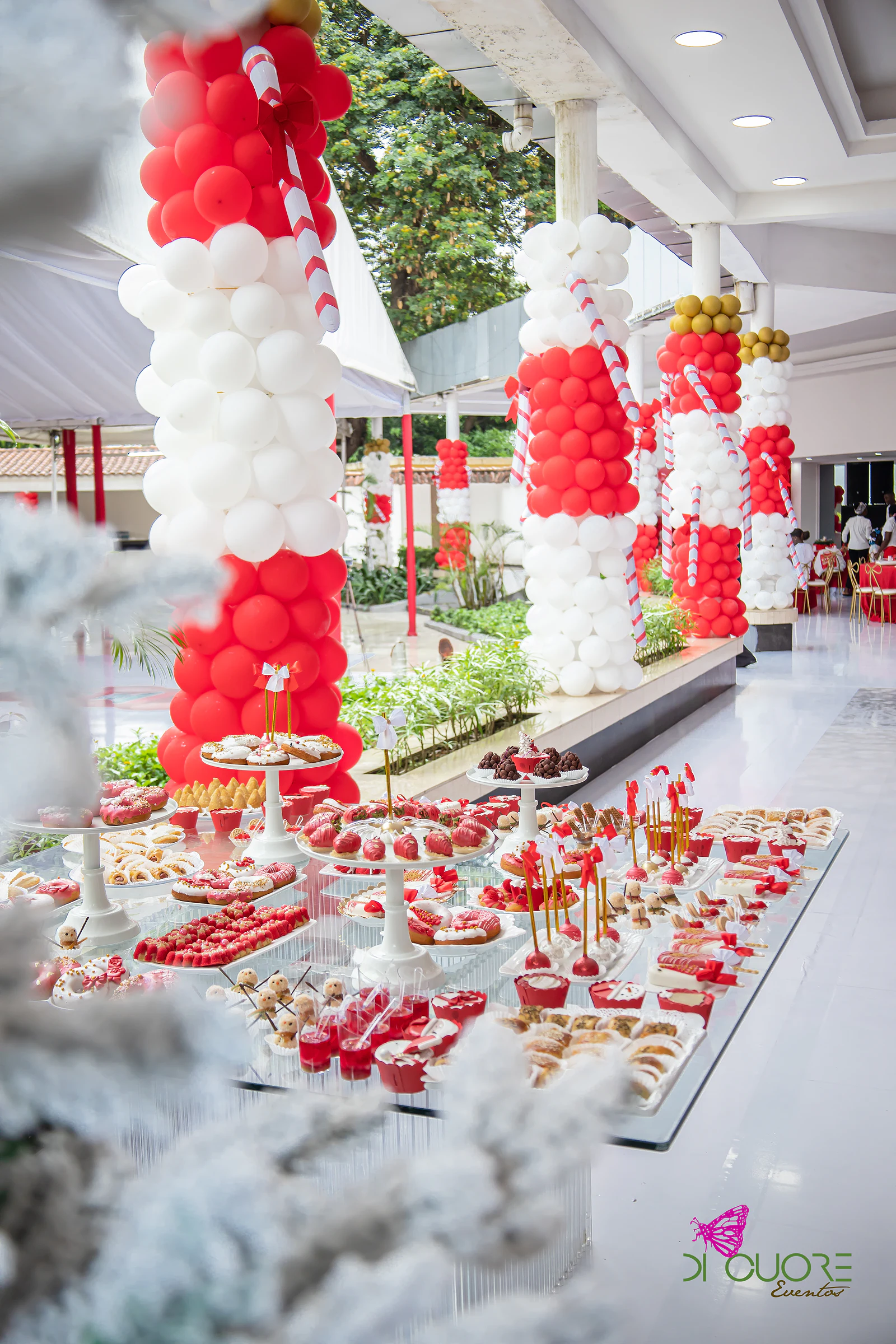 Christmas sweet table between columns of red and white balloons with candy canes, snow-dusted trees in the foreground
