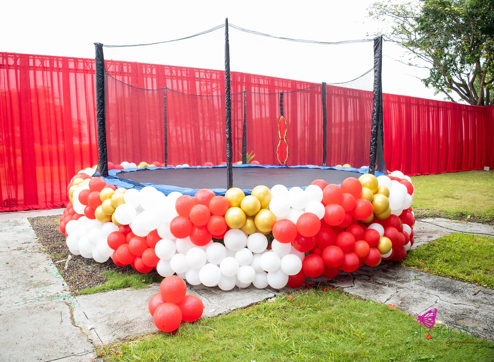 Trampoline ringed with a garland of red, white and gold balloons, before red drapes