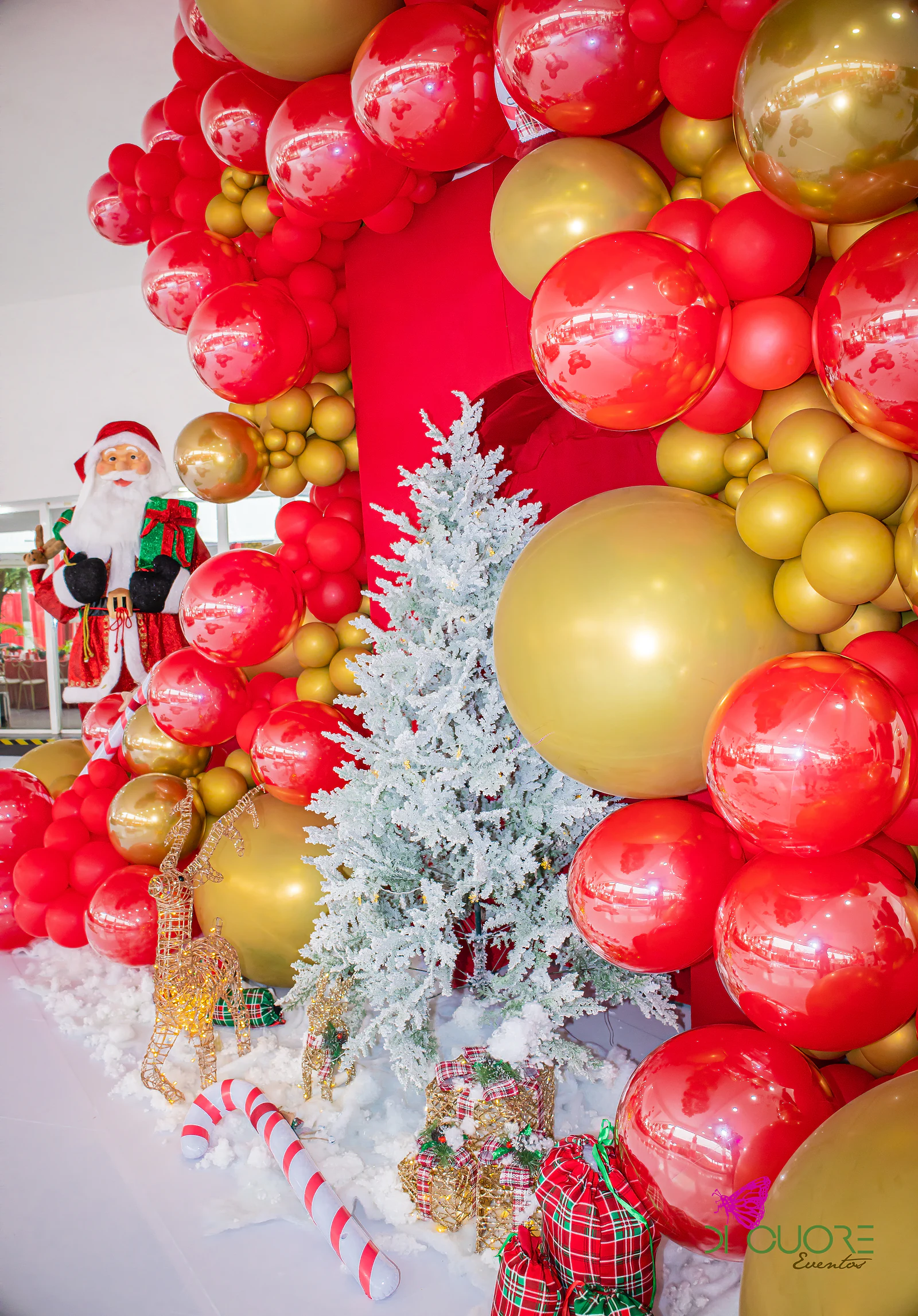 Close-up of the red and gold balloon sculpture, with a silver tree, a wire reindeer, candy canes and tartan gifts, and a Father Christmas figure behind
