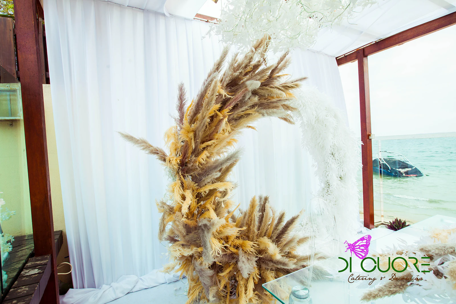 Close view of the arch of pampas grass and white leaves against the drapes, with the sea visible to the right
