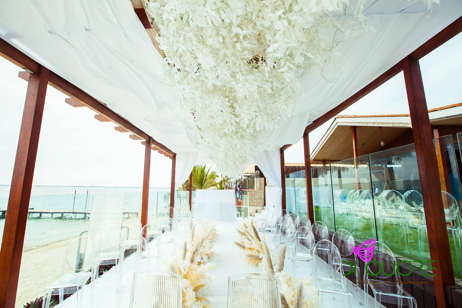 Ceiling of hanging white leaves above the aisle, with clear chairs, the beach and the sea on both sides